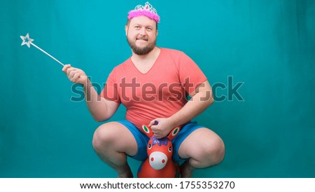 A  young bearded freaky man in a pink T-shirt with a diadem on his head riding a unicorn with a magic wand in his hand. A funny wizard joke to make and fulfill a wishg bearded freaky man in a