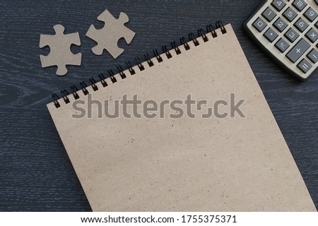Two cardboard puzzles, a calculator, and a spiral notebook on a dark background. Business, accounting of financial funds, business planning.