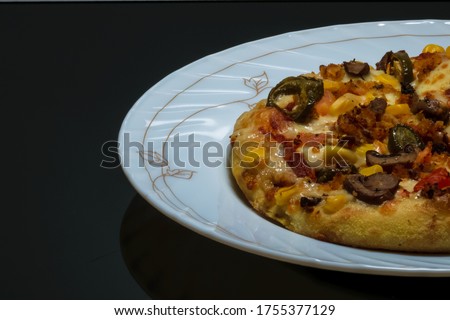 Vegetable pizza placed on a white plate and kept on a black table with space for text in the left