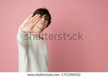 Young woman with making stop gesture with her palm outward, studio shot over pink background. Annoyed girl saying no, expressing denial, rejection or restriction. Negative human emotions, feelings Royalty-Free Stock Photo #1755386432