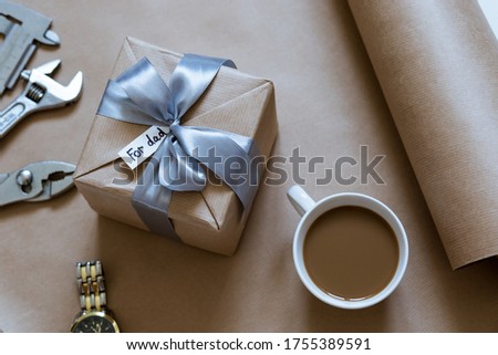 gift in craft packaging with a cup of coffee, a watch and accessories for repairs on the table for Father's Day