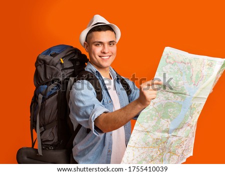 Active hiker with big backpack looking at city map, orange studio background
