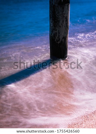 Seascape with single piling of ruined pier and soft flow of waves, long exposure photo