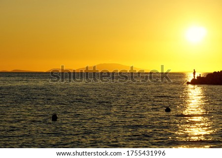 Silhouette of fisherman on the seacoast and mountain in the background of the beautiful summer sunset in yellow, beige and blue color tone