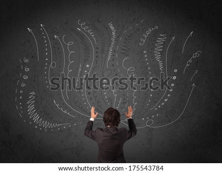 Thoughtful young businessman standing and deciding in front of a chalkboard with sketched arrows and lines in different directions