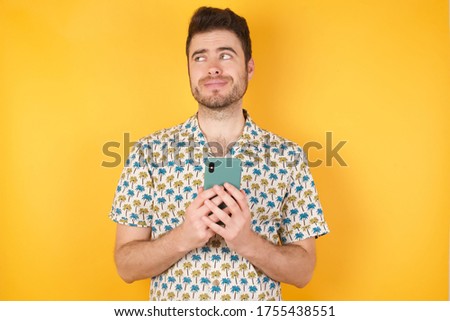 Photo of funny handsome Young man wearing hawaiian shirt holds telephone hands reads good youth news look empty space advert wear hawaiian shirt isolated yellow background