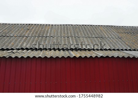 gray slate roof of a private house behind a red metal fence against the sky