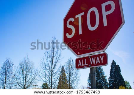 An image of a stop sign at an all way stop controlled intersection with blue sky and trees in the background in Oregon on a sunny Spring time morning.