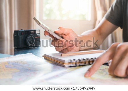 Man using smartphone and pointing to the map on the table