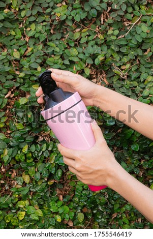 Aluminum thermos mug on hand with green leaves wall, stock photo