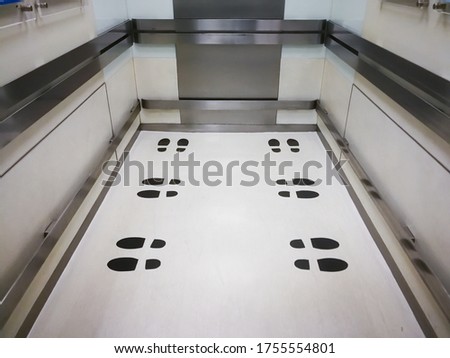 black footprint sticker on the elevator or lift floor with direction of standing position to limit or control number of people entry into the lift ,Social distancing in COVID-19,focus on the footprint
