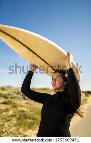 A vertical shot of an attractive female carrying a surfboard above her head in the middle of the road in Spain