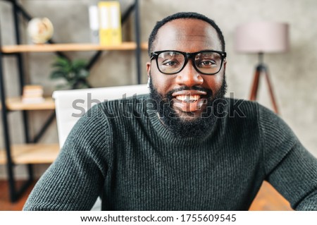 Webcam shot of African-American young guy in glasses, he looks into camera and smiles. Video screen, video chat, online call Royalty-Free Stock Photo #1755609545