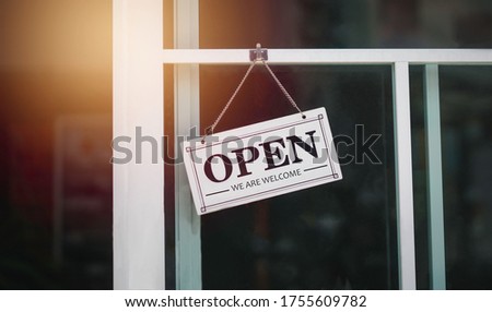 A sign hanging front  of a coffee shop or cafe that says the word "Open we are Welcome" On Window with colorful bokeh light abstract background small business concept.