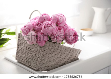 Basket with beautiful pink peonies in kitchen