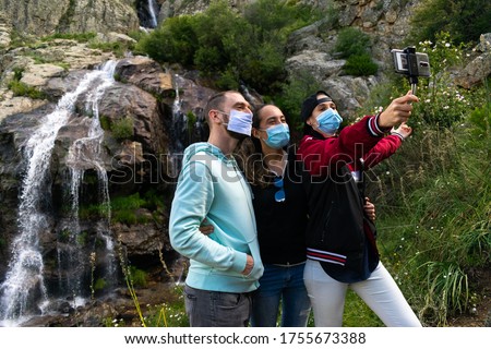 Caucasian people taking a selfie wearing mask in a waterfall in the nature. Group of people travelling around Europe during the coronavirus (covid 19) health crisis wearing sanitary mask. Eco turism Royalty-Free Stock Photo #1755673388