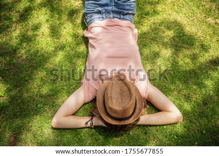 Free woman enjoying nature lying on grass with hat on face. Summer sunny day