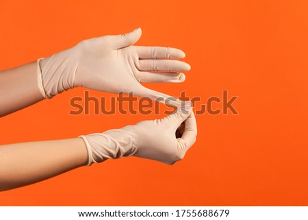 Profile side view closeup of human hand in white surgical gloves showing how to take of gloves. indoor, studio shot, isolated on orange background.