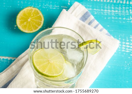 Cold summer delicious coctail with lime and ice in a glass with drops on the white and blue background.