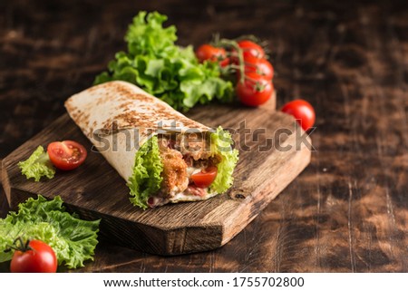 Concept of street fast food - Roll with chicken and fresh cherry tomatoes and lettuce on a wooden Board on a dark background. Close-up with copy space. Horizontal orientation. Royalty-Free Stock Photo #1755702800