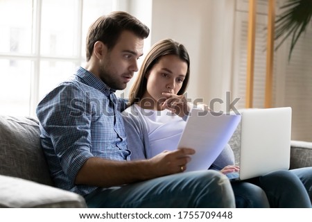 Shocked worried young couple reading documents, financial problems, using laptop, online banking service, checking mortgage or insurance contract terms, calculating domestic bills or taxes Royalty-Free Stock Photo #1755709448