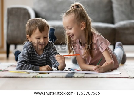 Happy little girl and boy drawing with colorful pencils in album at home, preschool sister and brother enjoying leisure time, playing together on warm floor with underfloor heating in living room