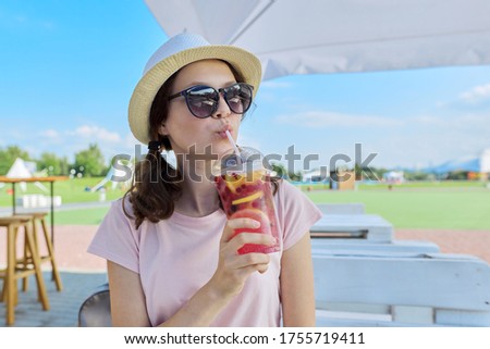 Teens, lifestyle, summer, vacation. Girl in audor cafe in hat sunglasses with berry drink.