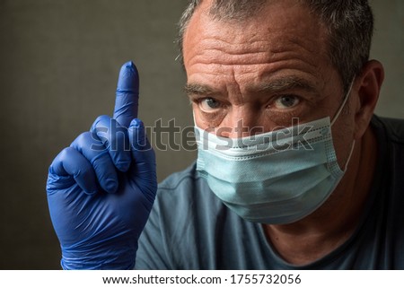 Adult man in a medical mask shows a finger up, close-up face