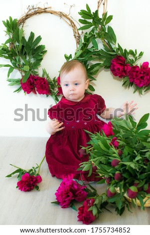 Little cute girl 1 year old in a dress of Marsala color with a wicker basket with peonies. Spring and flowers. Children's fashion
