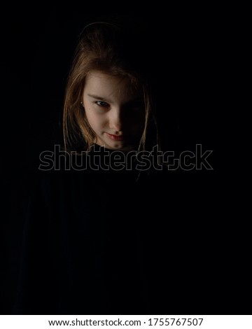 A girl in a black shirt on black background is looking in camera. Copy space