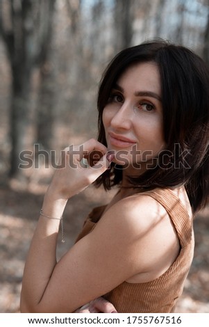 A beautiful young woman holds her hand at her face and looks into the camera. Portrait. Sunny summer day. Close up