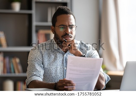 African student guy sit at desk hold papers tasks having difficulties with test, company lawyer read contract terms and detail feels discontented, received bad news from bank unpleasant letter concept Royalty-Free Stock Photo #1755781052
