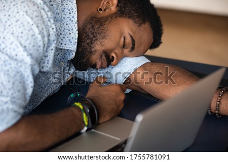 Close up image African male worker falls asleep at desk lie at workplace table overwhelmed with computer work. Chronic fatigue, lack of energy, unmotivated employee or lazy student and boredom concept