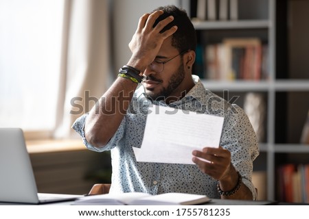 Stressed african businessman sit at desk hold paper letter reading bad awful negative news got fired from work. Dismissal notice, financial problems debt notification from bank, unpaid invoice concept Royalty-Free Stock Photo #1755781235