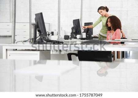 Two young women at desk one pointing at computer monitor