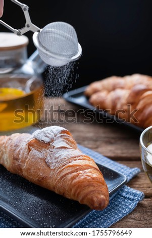 French baked croissants sprinkled with icing or powered sugar on wooded table background. Eating croissant with tea in café is healthy. Croissant is pastry served in café. Healthy lifestyle concept.