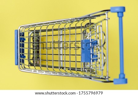 Small empty supermarket grocery push cart for shopping toy with wheels isolated on yellow minimal background. 