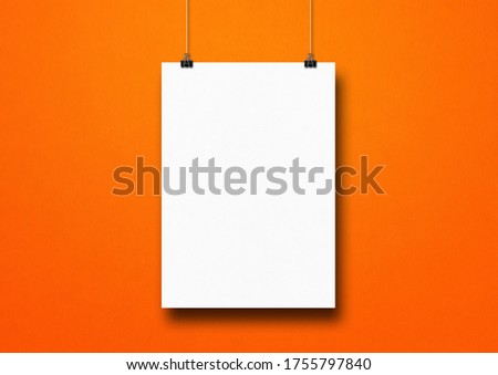 White poster hanging on an orange wall with clips. Blank mockup template