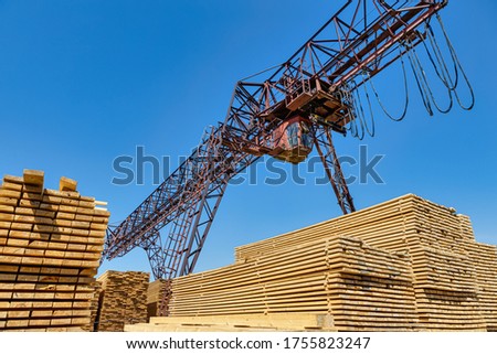 Industrial warehouse timber mill, finished products on a sawmill outdoors. Timber loading Gantry crane. Royalty-Free Stock Photo #1755823247