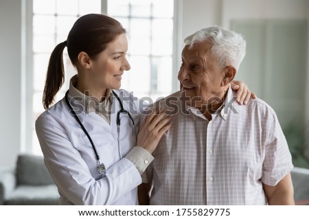 Head shot portrait smiling caring female doctor hugging older man, standing together, young woman caregiver wearing white coat and stethoscope supporting mature senior patient, healthcare concept