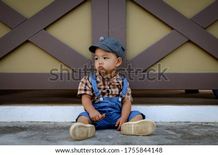 Lonely and unhappy 1 year old cute toddler Asia boy kid in bib jeans sitting and holding food in boring emotion. Lonely kid, bored of food and emotion concept.