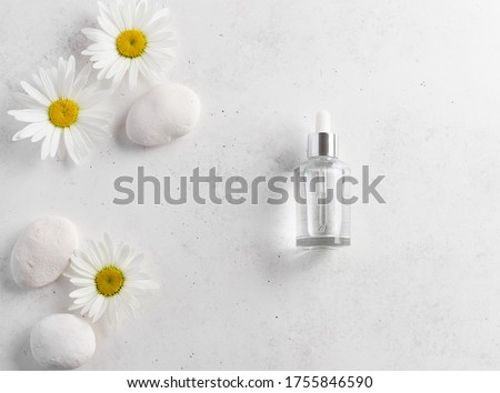 glass bottle with cosmetic serum on a white background with fresh daisies and stones. beauty concept. Template for advertising. place for your text. flat lay. horizontal image