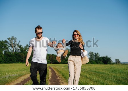 Happy family walking on a track on a beautiful sunny day in a countryside. Parents holding baby's hands, swinging him back and forth
