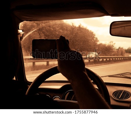 silhouette of man hand with mobile cell phone to take a photo or video of car rearview mirror. one hand turns the steering wheel