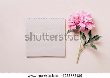 Notebook and beautiful pink peony on beige background. Spring or summer floral background.
