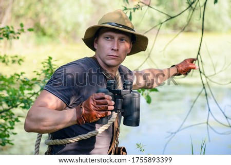 Adventurer man in hat with binoculars in hand is showing a way.