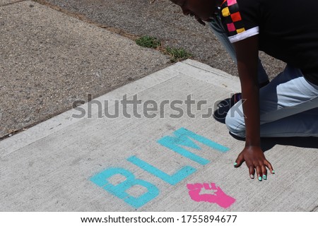Child kneeling near BLM Blaack Lives Matter words on Sidewalk