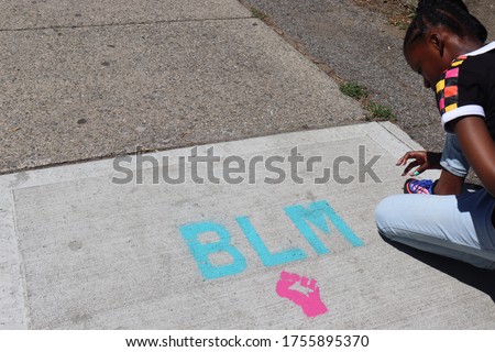 Girl kneeling near BLM for Black Lives Matter Sign with fist symbol 