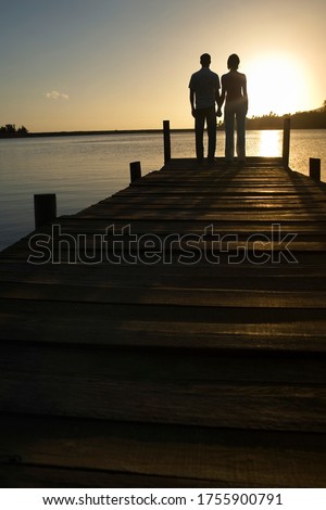 Couple standing on dock by lake holding hands back view