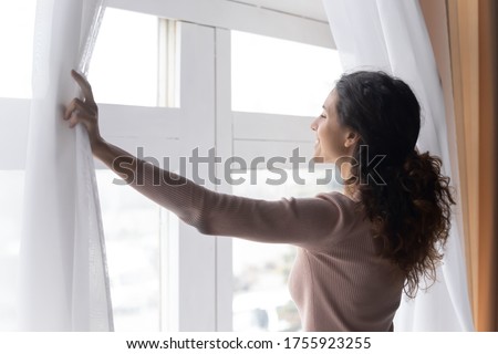 Close up smiling woman opening curtains in morning, enjoying sunlight, standing at home, happy overjoyed young female looking out window, dreaming, starting new day, planning good future Royalty-Free Stock Photo #1755923255